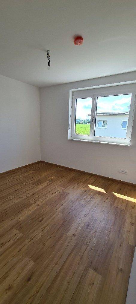 Freundliches Zimmer mit Laminatboden und großem Fenster, das viel Tageslicht hereinlässt.