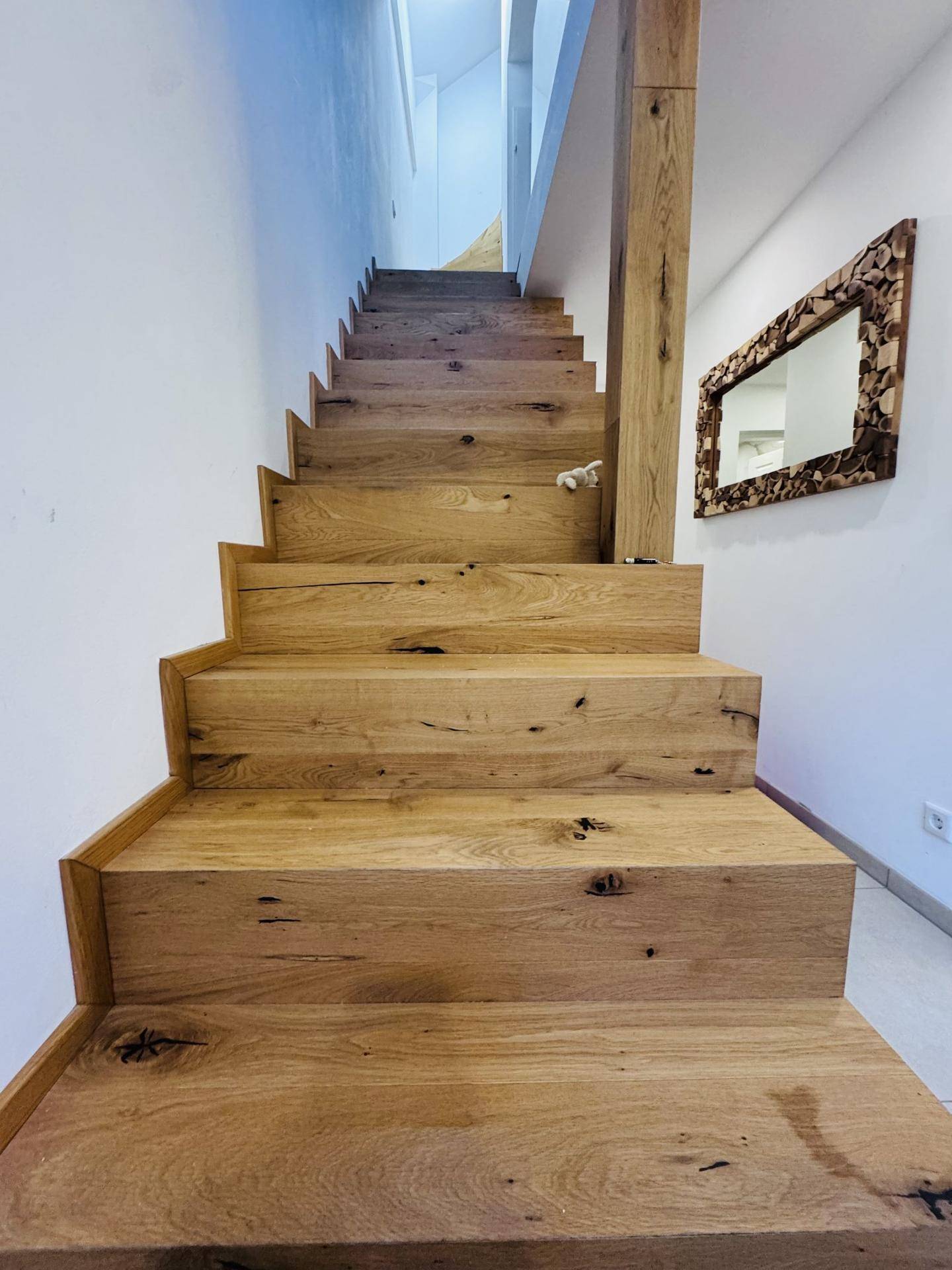 Elegante Holztreppe mit natürlicher Maserung und einem dekorativen Spiegel an der weißen Wand.