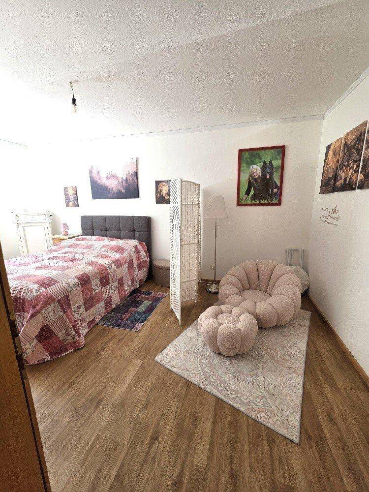 Gemütliches Schlafzimmer mit Holzboden, einem Doppelbett und modernen, weichen Sitzmöbeln.