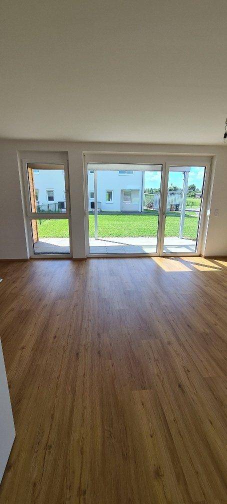 Heller Wohnbereich mit großen Fenstern und Zugang zum Garten, ausgestattet mit Holzboden.