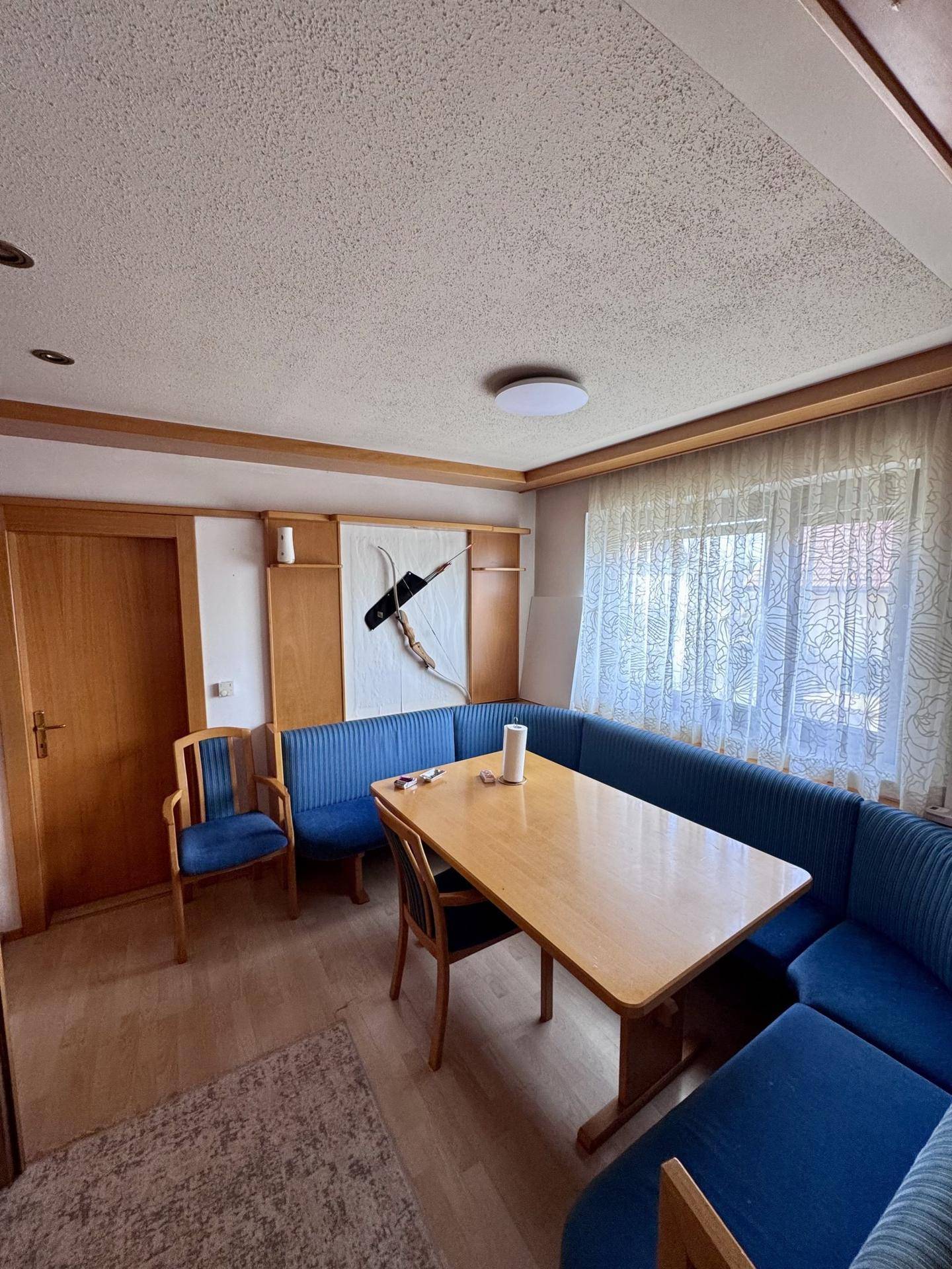Heller Essbereich mit Holztisch, blauer Eckbank und Fenster mit Vorhängen.