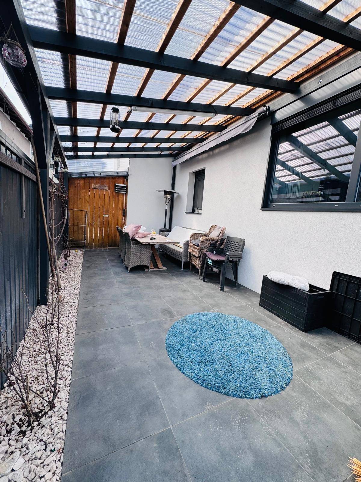 Überdachte Terrasse mit Sitzgelegenheiten und Kiesbeet, ideal für entspannte Stunden im Freien.