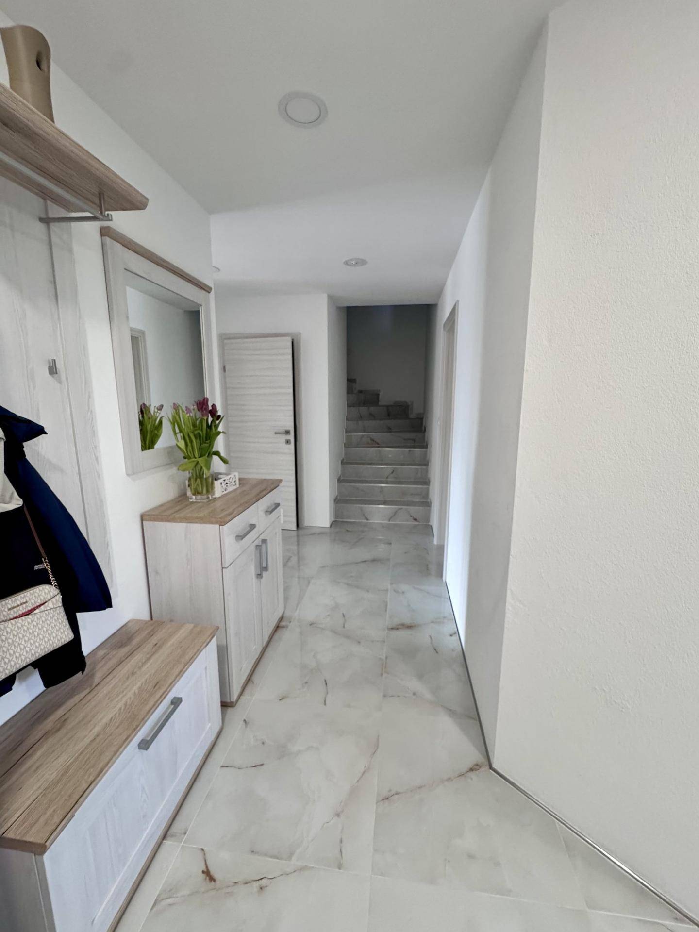 Eingangsbereich mit Marmorfliesen, Garderobe und Spiegel, der zu einer Treppe führt.