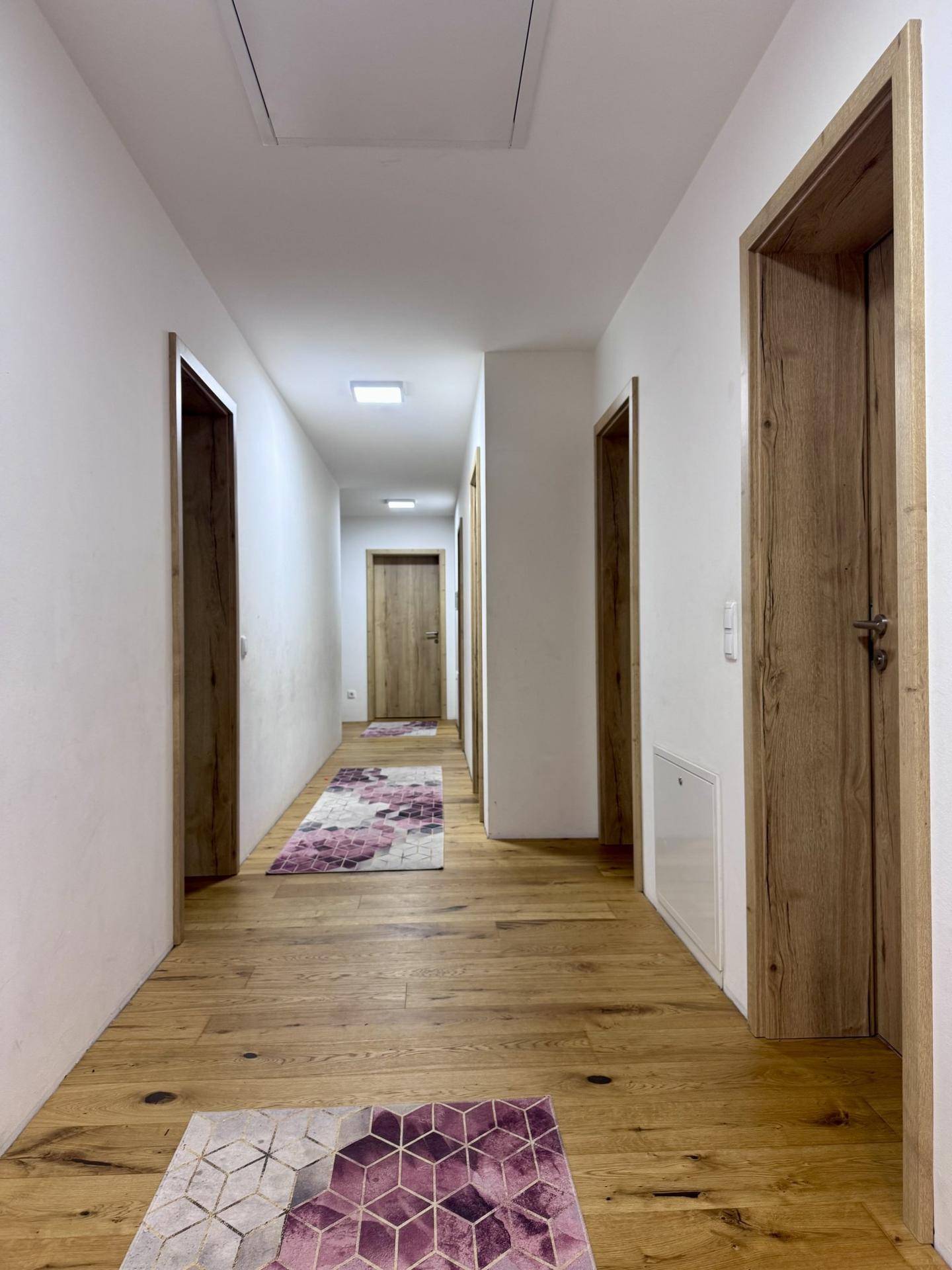 Heller Flur mit Holzboden, weißen Wänden und mehreren Holztüren, die zu den Zimmern führen.