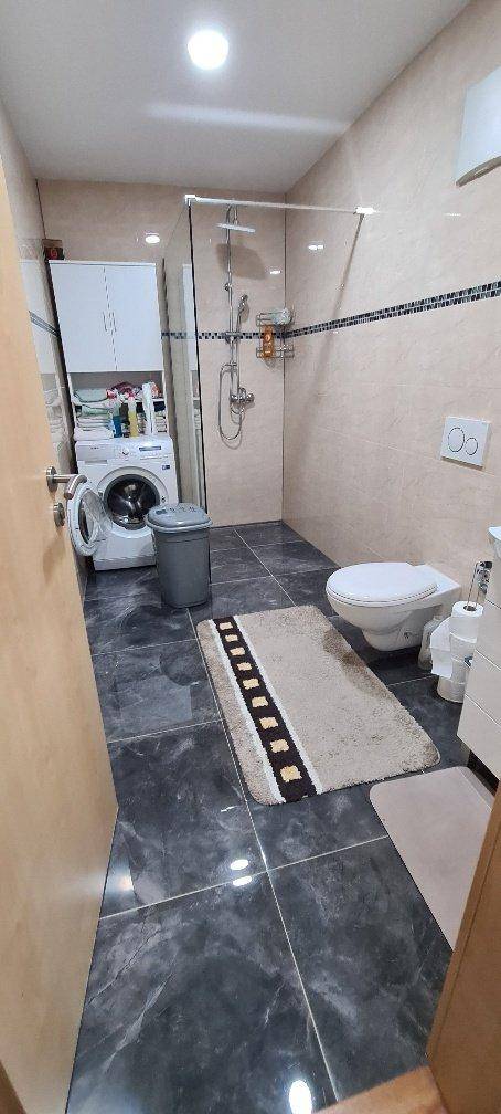 Modernes Badezimmer mit Dusche, WC und Waschmaschine, gefliest in dunklem Grau.