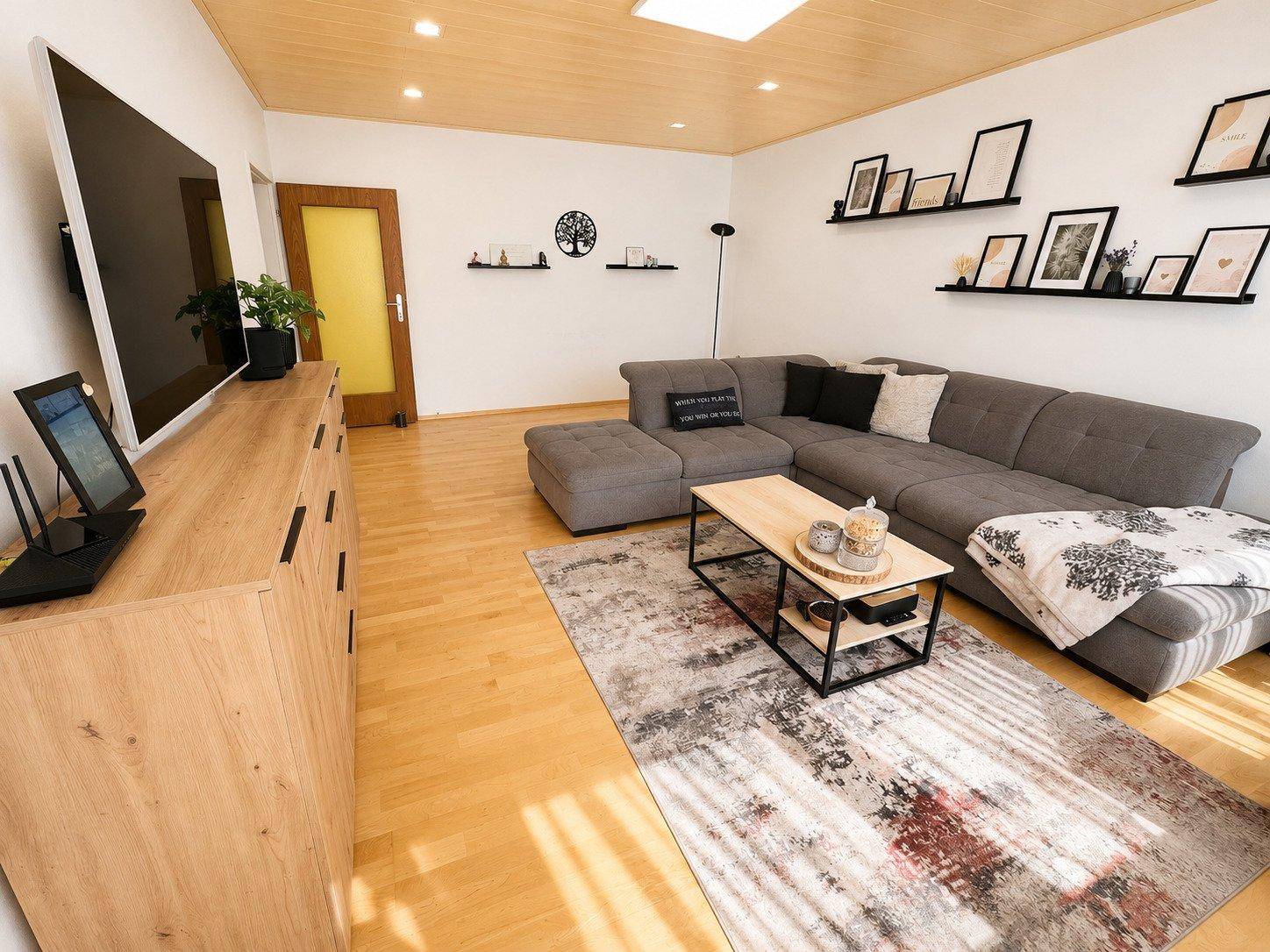 Geräumiges Wohnzimmer mit Holzdecke, bequemer Couch, Holzboden und moderner Einrichtung.