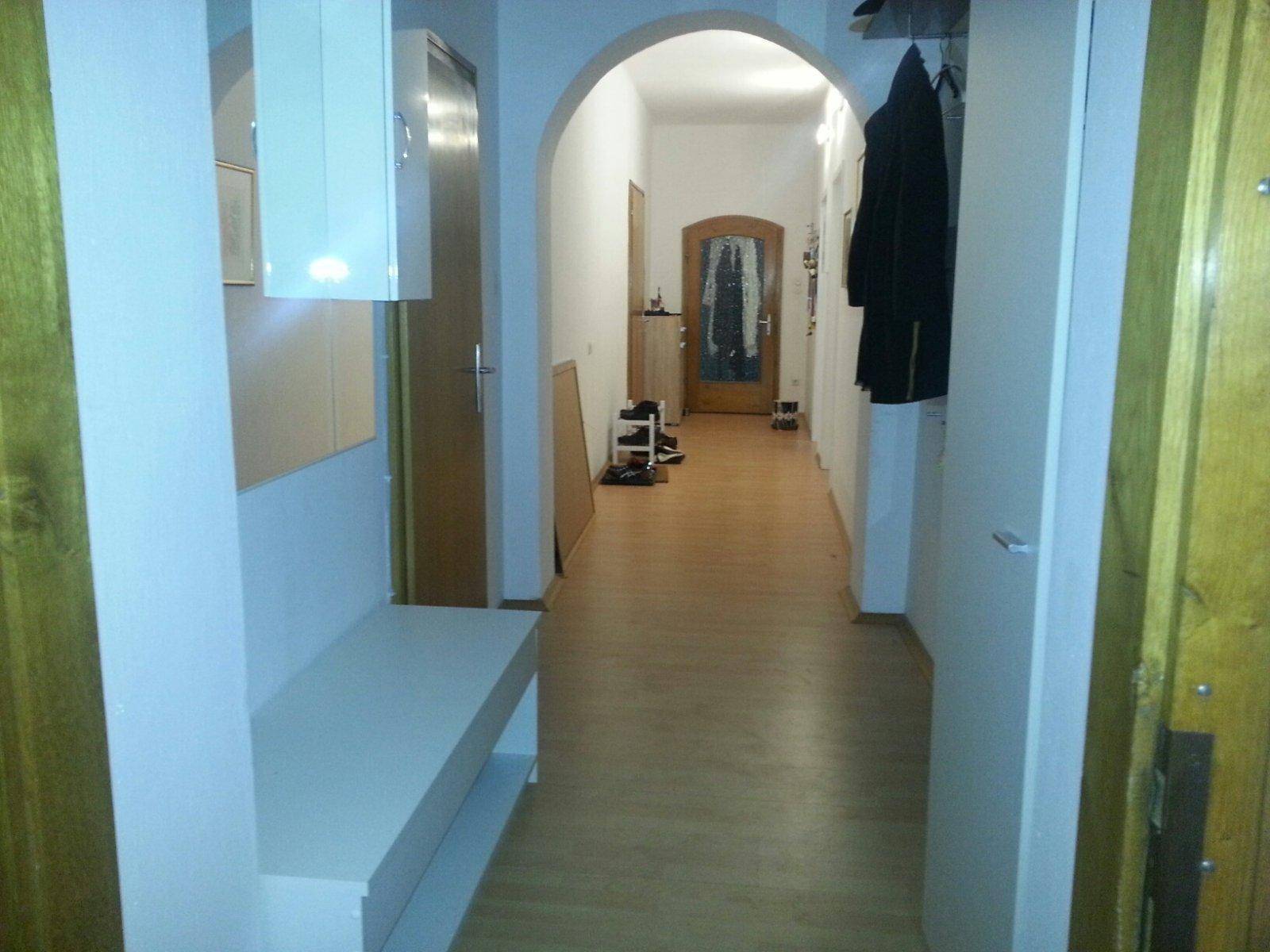 Heller Flur mit Holzboden, Garderobe und einem Bogen zum nächsten Bereich.