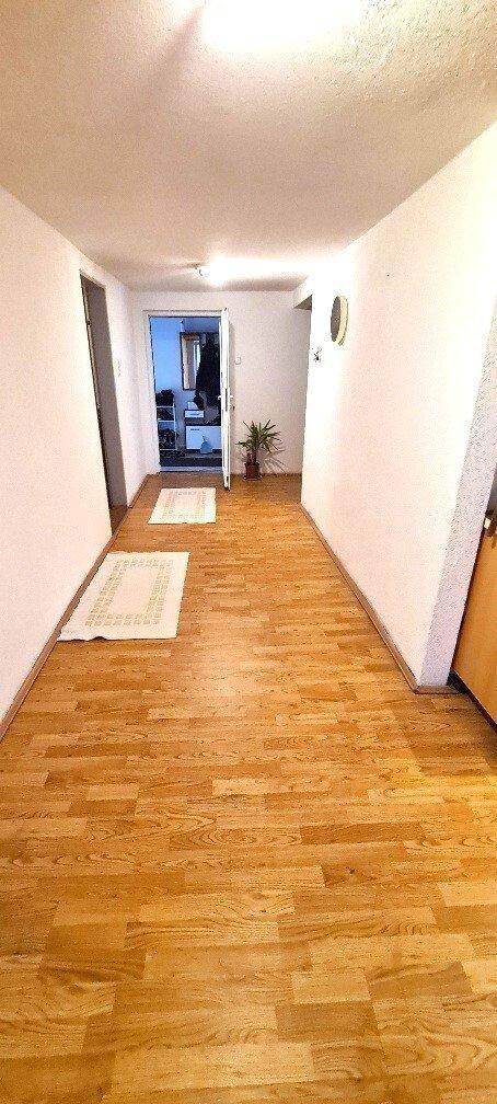 Langer, heller Flur mit Parkettboden und weißen Wänden, der zu weiteren Räumen führt.