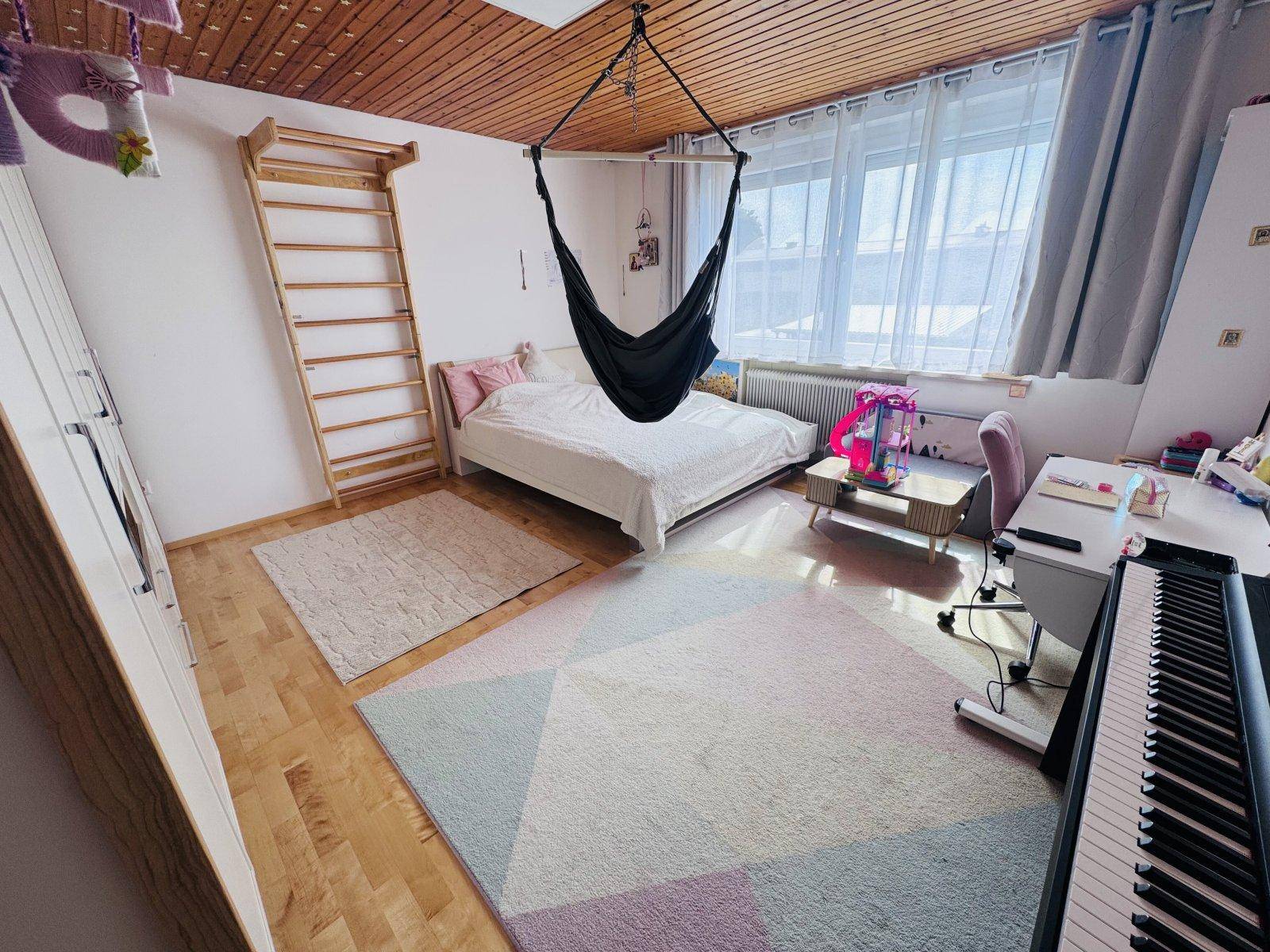 Helles Schlafzimmer mit Holzboden, Sprossenwand, Schaukel und großem Fenster.