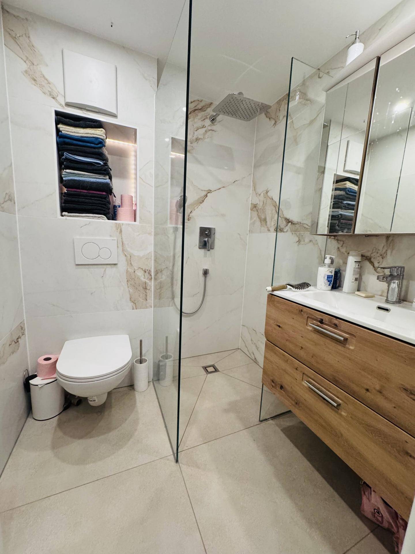 Modernes Badezimmer mit begehbarer Dusche, wandhängendem WC und eleganten Marmorfliesen.