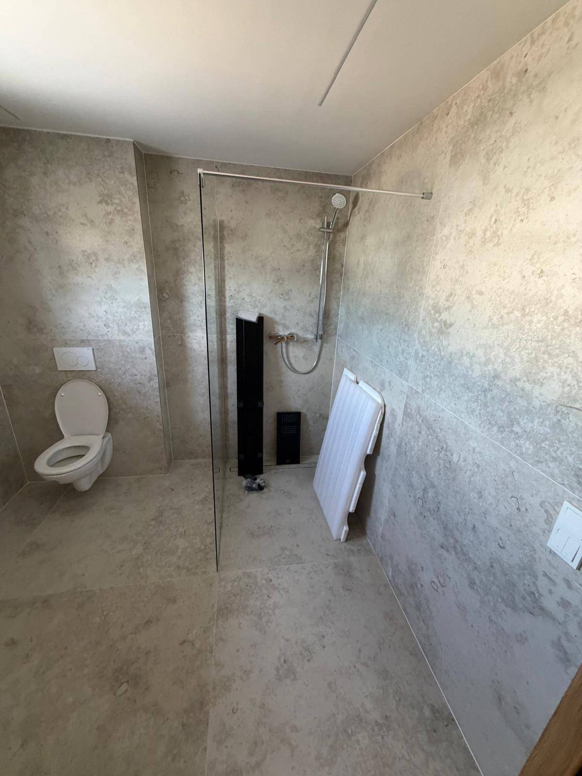 Geräumiges Badezimmer mit wandhängendem WC, begehbarer Dusche und großformatigen Fliesen.