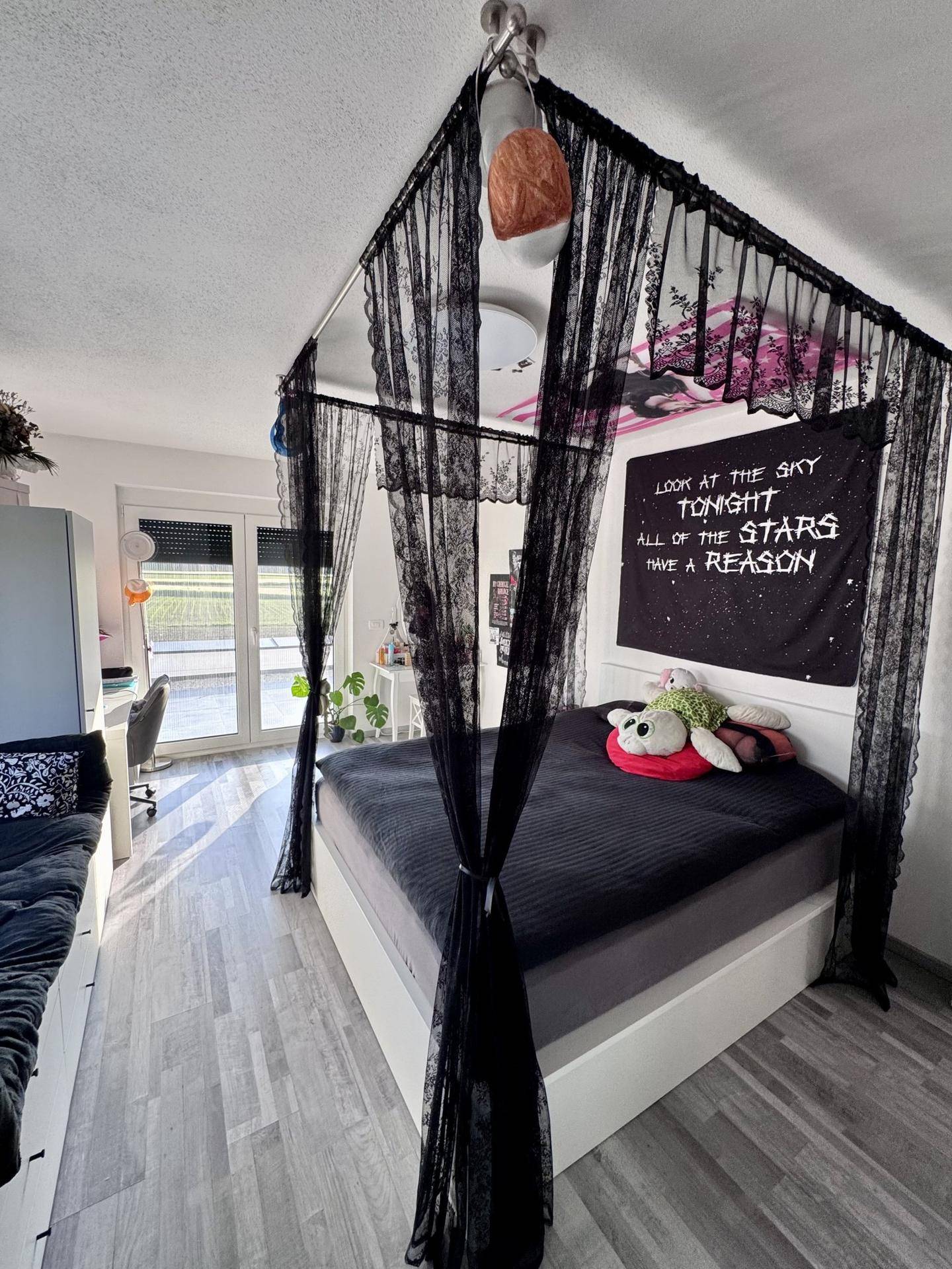 Schlafzimmer mit Himmelbett und dunklem Vorhang, Schreibtisch und Zugang zum Außenbereich.