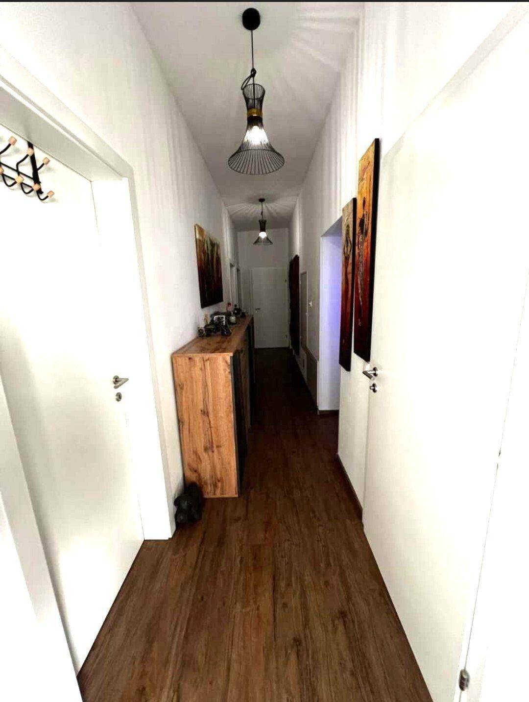 Langer, heller Flur mit Holzboden und modernen Wanddekorationen, der zu weiteren Räumen führt.