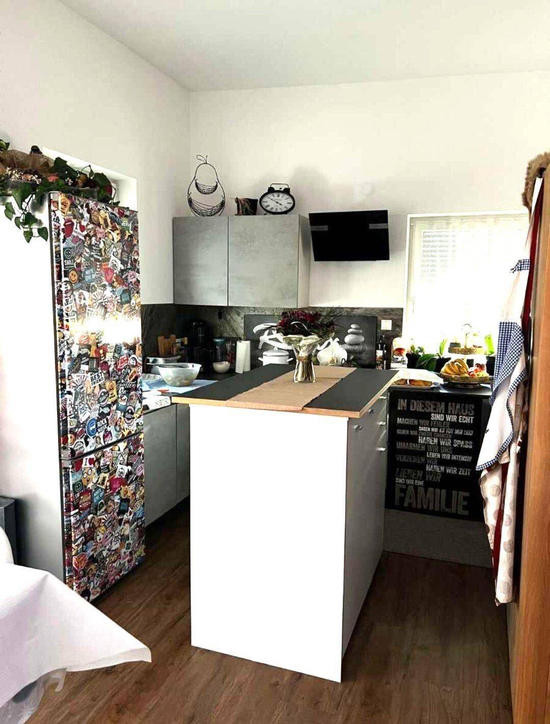 Kompakte Küche mit Kücheninsel, modernen grauen Schränken und einem auffällig dekorierten Kühlschrank.