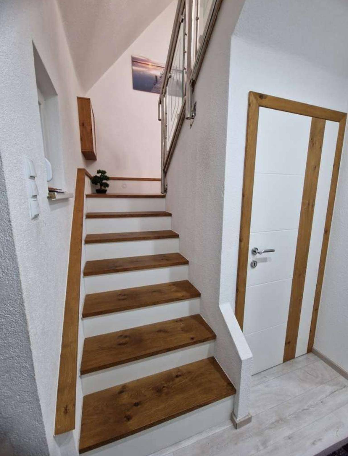 Heller Flur mit Holztreppe, modernem Geländer und weißer Holztür.
