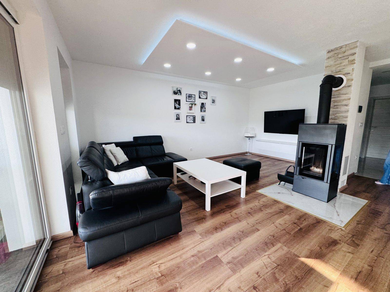 Modernes Wohnzimmer mit dunklem Sofa, Holzboden und einem stilvollen Kaminofen als Blickfang.