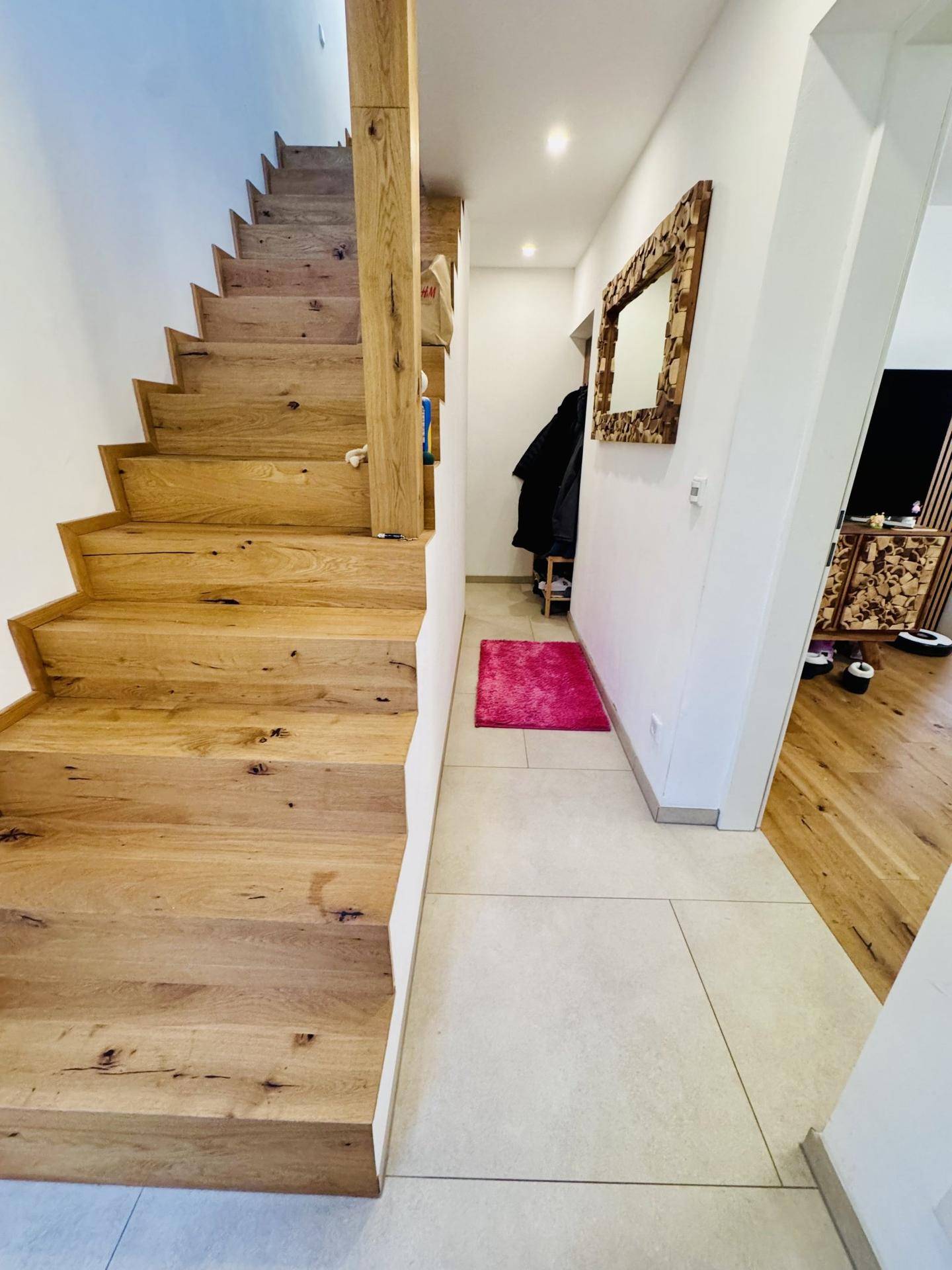 Heller Flur mit Holztreppe, Fliesenboden und einem dekorativen Spiegel an der Wand.