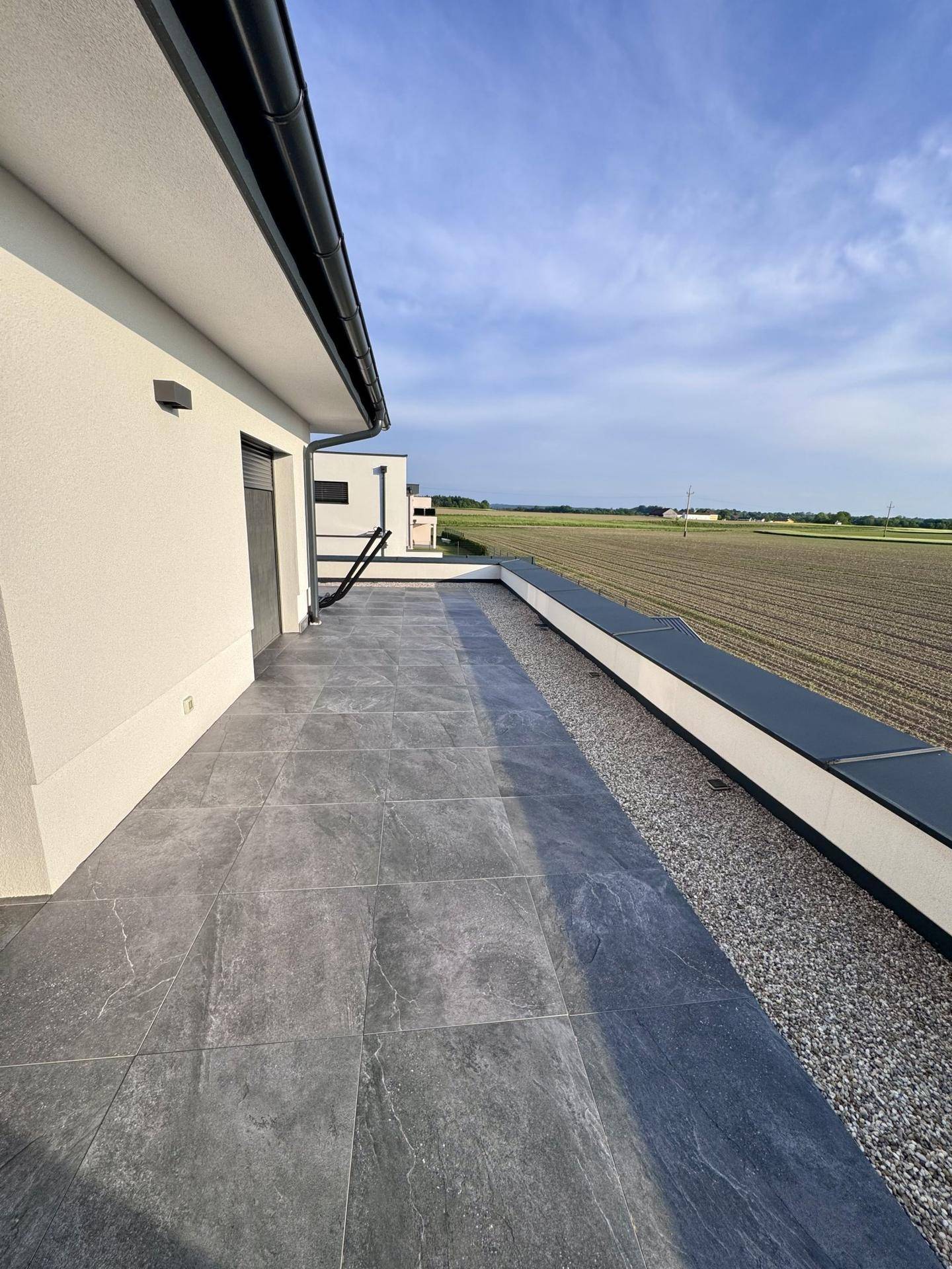 Lange Terrasse mit Fliesenboden und weitem Blick über die ländliche Umgebung.