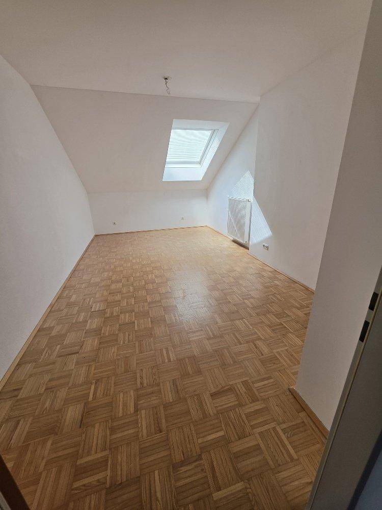 Helles Zimmer mit Parkettboden, Dachschräge und einem großen Dachfenster für viel Licht.