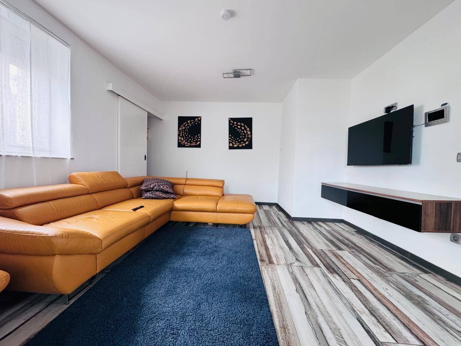 Helles Wohnzimmer mit auffälligem gelbem Ledersofa und Wandfernseher.