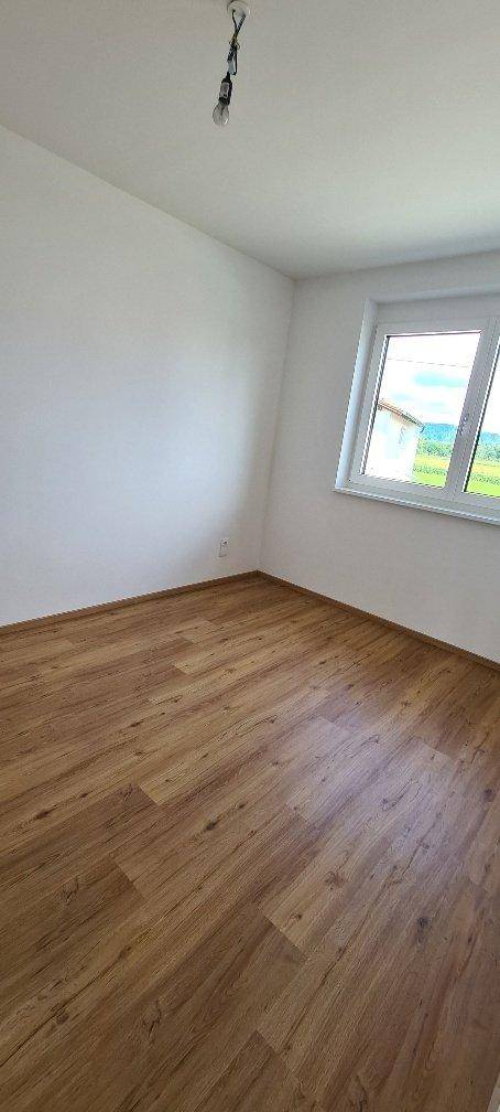 Helles Schlafzimmer mit Laminatboden und Fenster mit Blick ins Grüne.