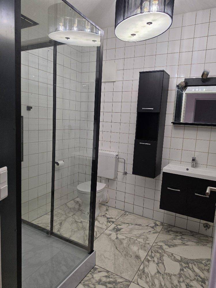 Badezimmer mit Duschkabine, WC, Einzelwaschbecken und dunklen Schränken auf gefliestem Boden.