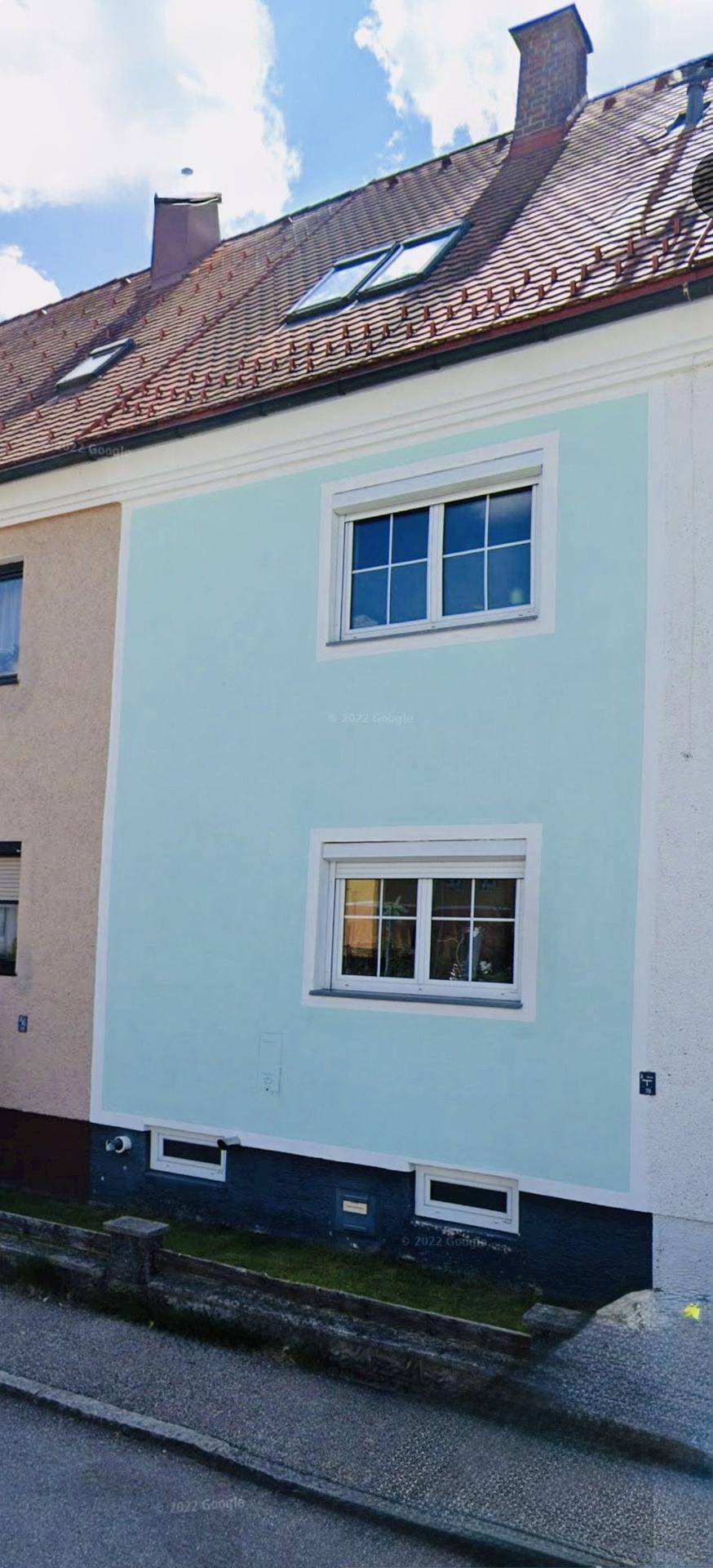 Fassade eines Wohnhauses mit hellblauer Farbgebung, weißen Fenstern und Dachfenstern im Ziegeldach.