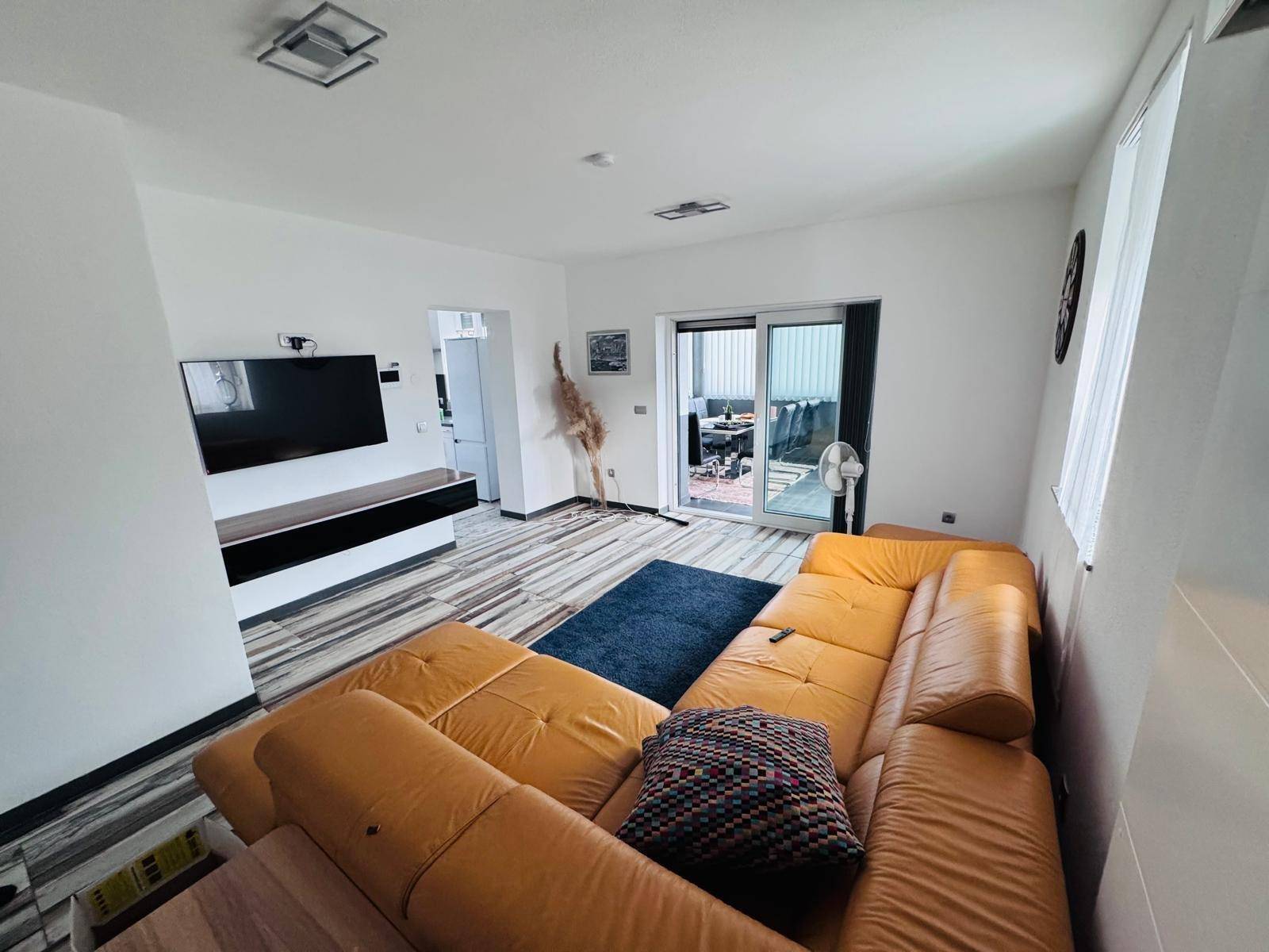 Geräumiges Wohnzimmer mit gelbem Sofa und Schiebetür zum Außenbereich.