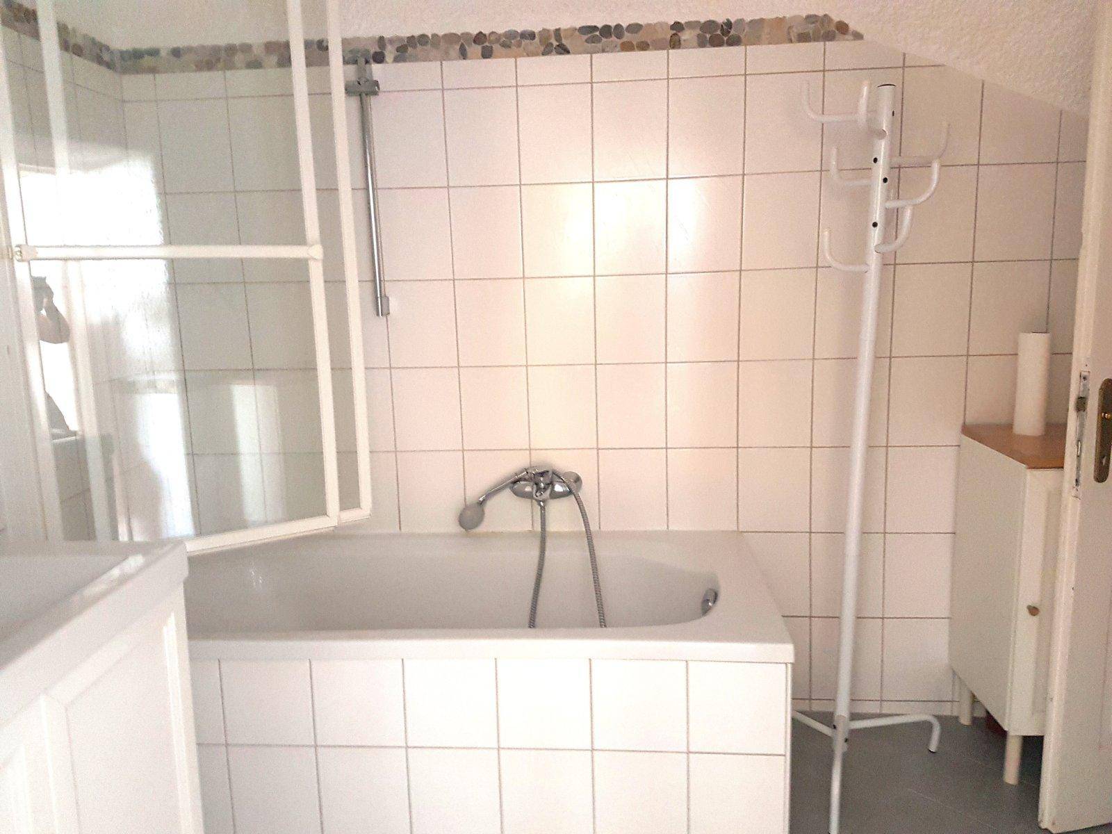 Helles Badezimmer mit Badewanne, weißen Fliesen und Dachschräge.