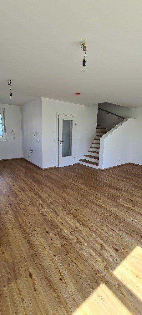 Geräumiger Wohnbereich mit Laminatboden und offener Treppe zum Obergeschoss.