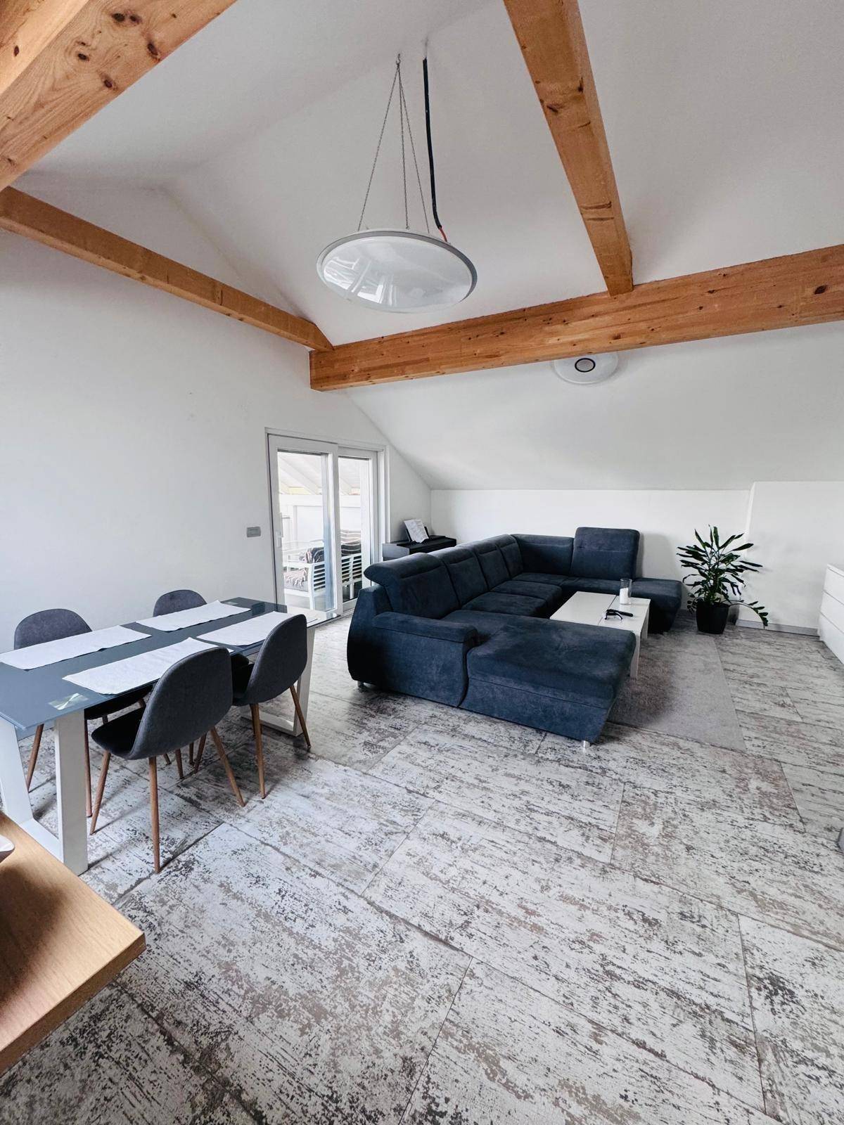 Offener Wohn-Essbereich mit sichtbaren Holzbalken und Zugang zur Dachterrasse.