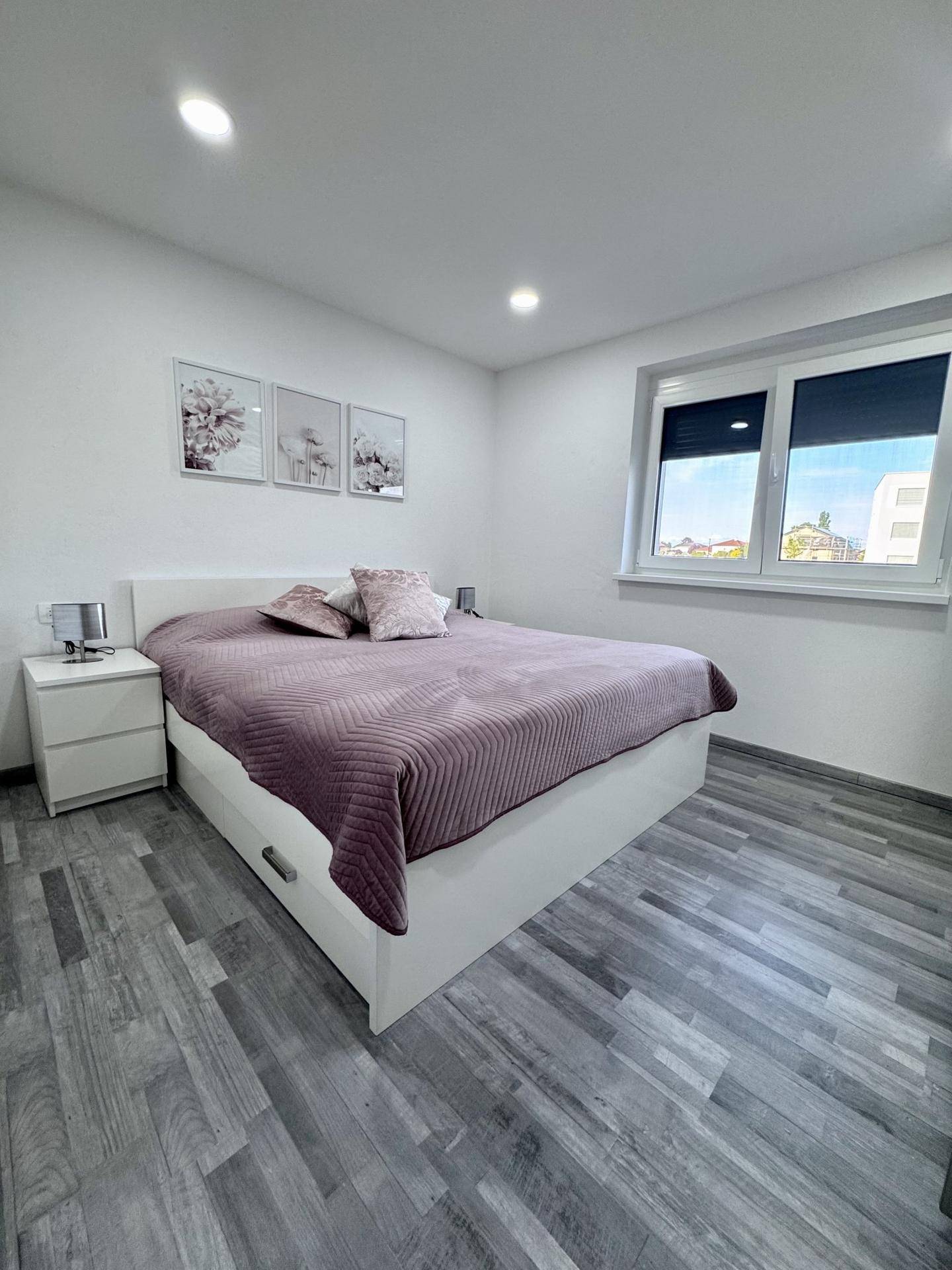 Gemütliches Schlafzimmer mit Doppelbett, Laminatboden und einem Fenster mit Rollladen.