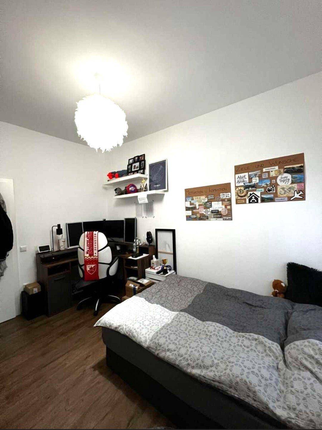 Schlafzimmer mit Doppelbett, Schreibtisch und Computern, dekoriert mit persönlichen Elementen.