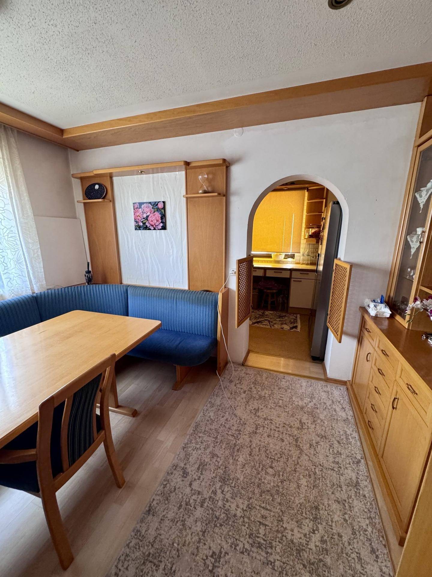 Essbereich mit Holztisch und blauer Eckbank, angrenzend an die Küche durch einen Bogen.
