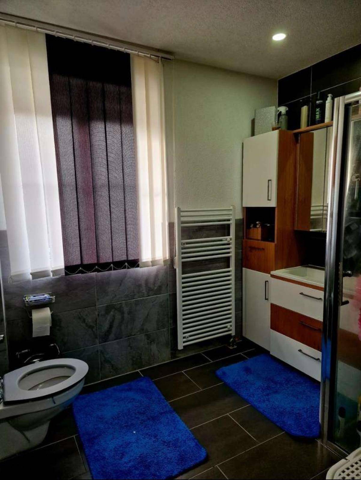 Modernes Badezimmer mit Dusche, WC, Fenster und beheiztem Handtuchhalter.