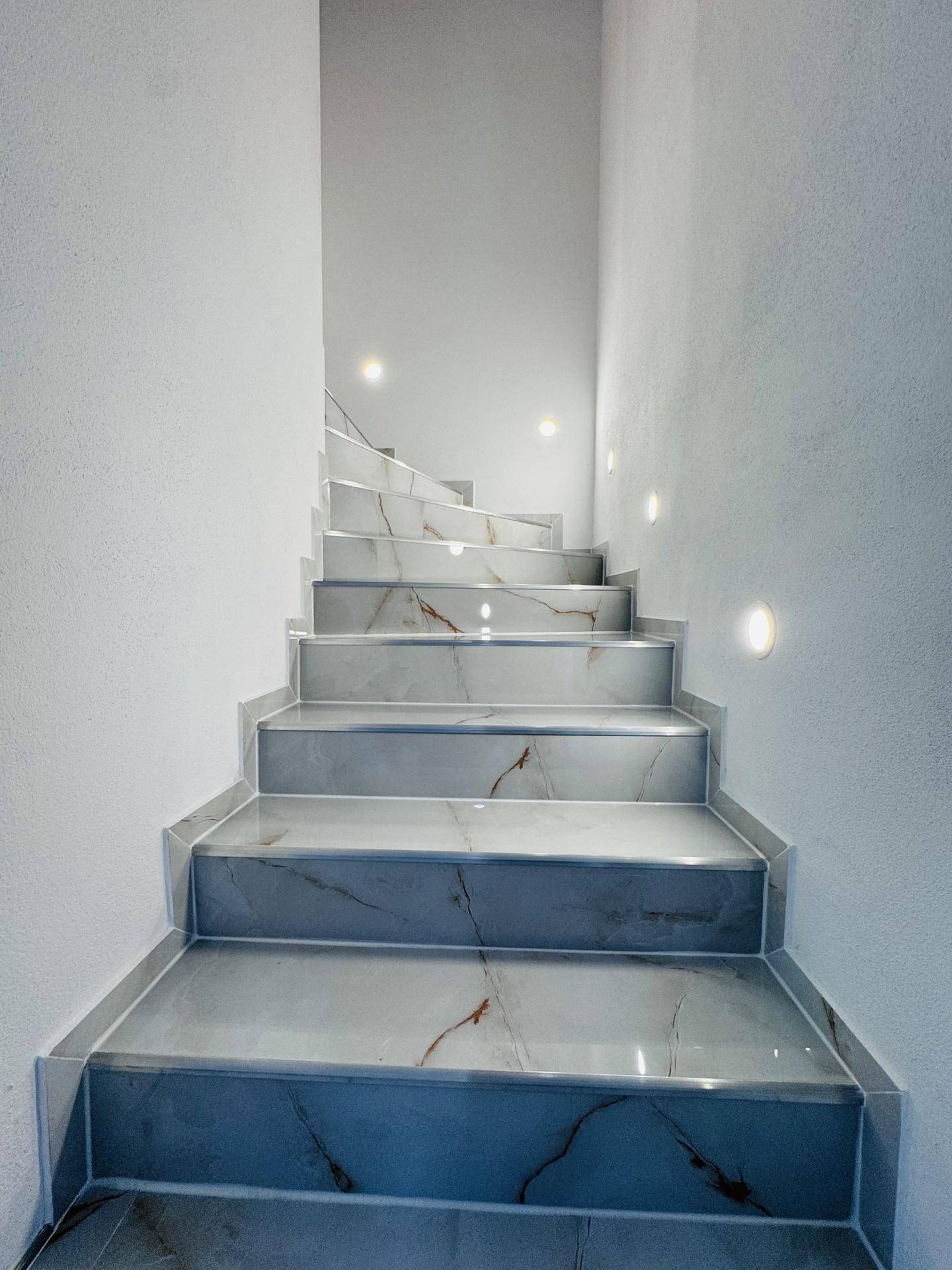 Elegante Treppe mit Marmorfliesen und indirekter Beleuchtung, die in die obere Etage führt.