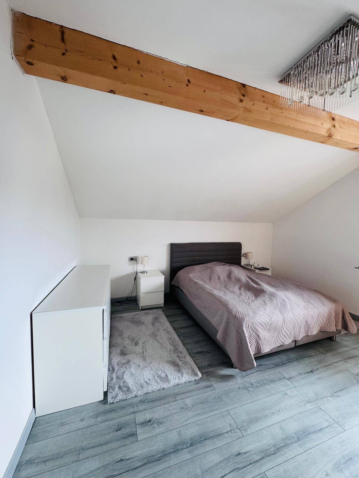 Gemütliches Schlafzimmer im Dachgeschoss mit sichtbarem Holzbalken und schräger Decke.