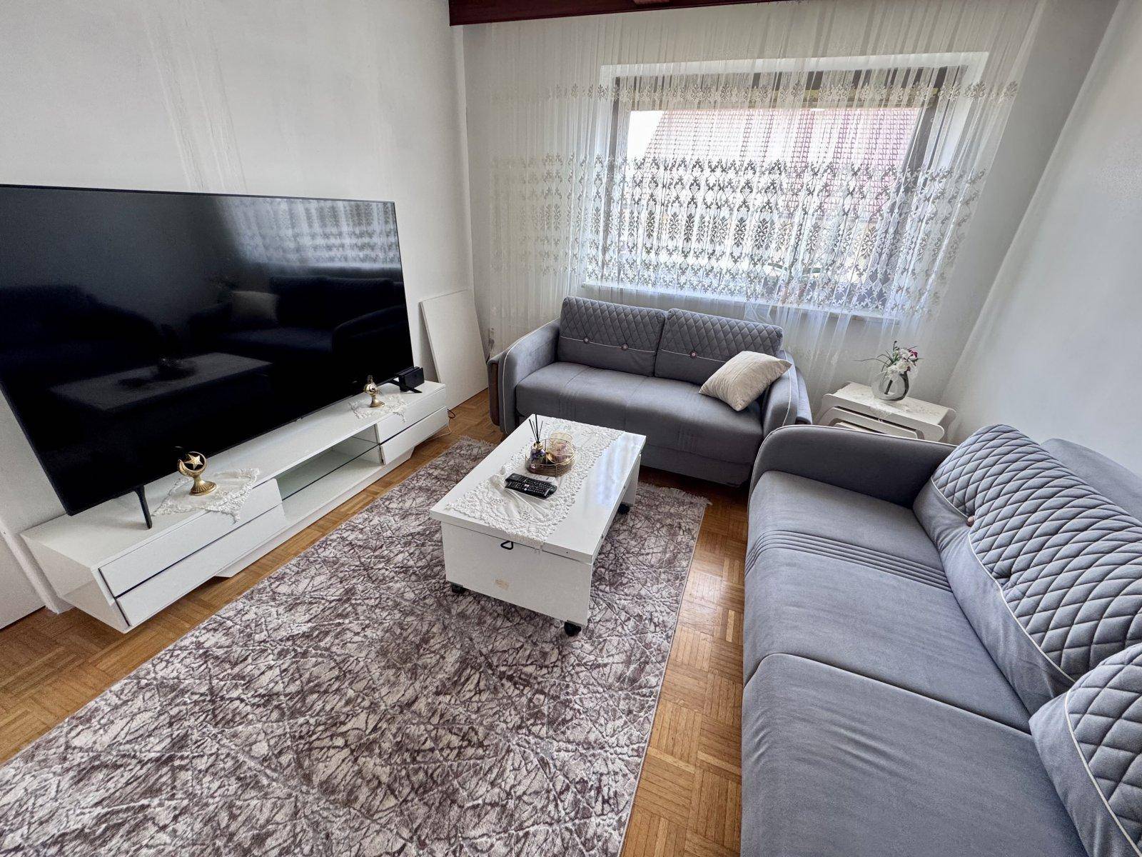 Gemütliches Wohnzimmer mit zwei grauen Sofas, großem Fernseher und Parkettboden.
