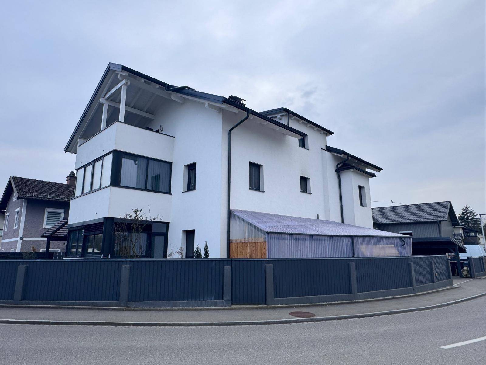 Moderne Wohnhausfassade mit großen Fenstern und einem überdachten Bereich.