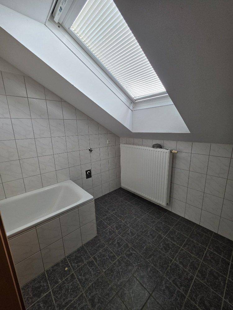 Badezimmer mit Badewanne, Fliesen, Dachschräge und einem Dachfenster für natürliches Licht.