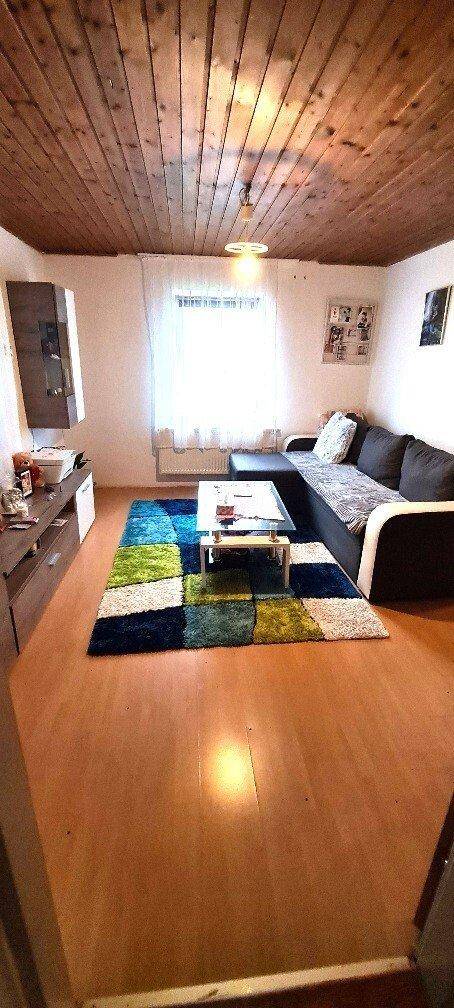 Gemütliches Wohnzimmer mit Sofa, Couchtisch, farbigem Teppich und Holzdecke.