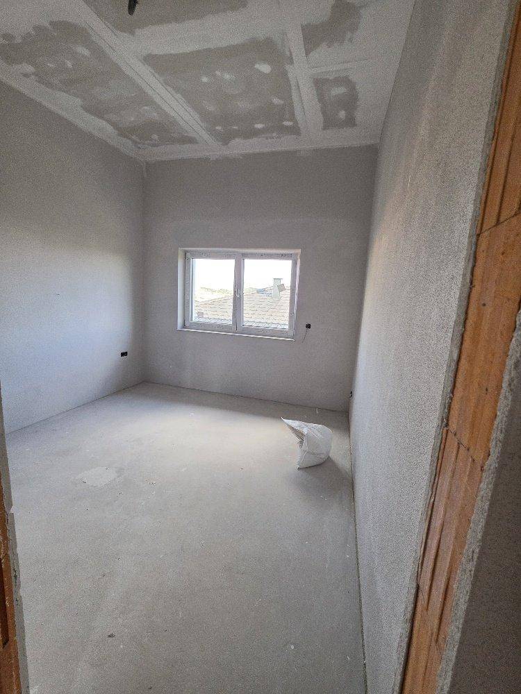 Unfertiger Raum mit Betonboden, Rohbauwänden und einem Fenster, das Tageslicht in den zukünftigen Wohnbereich bringt.