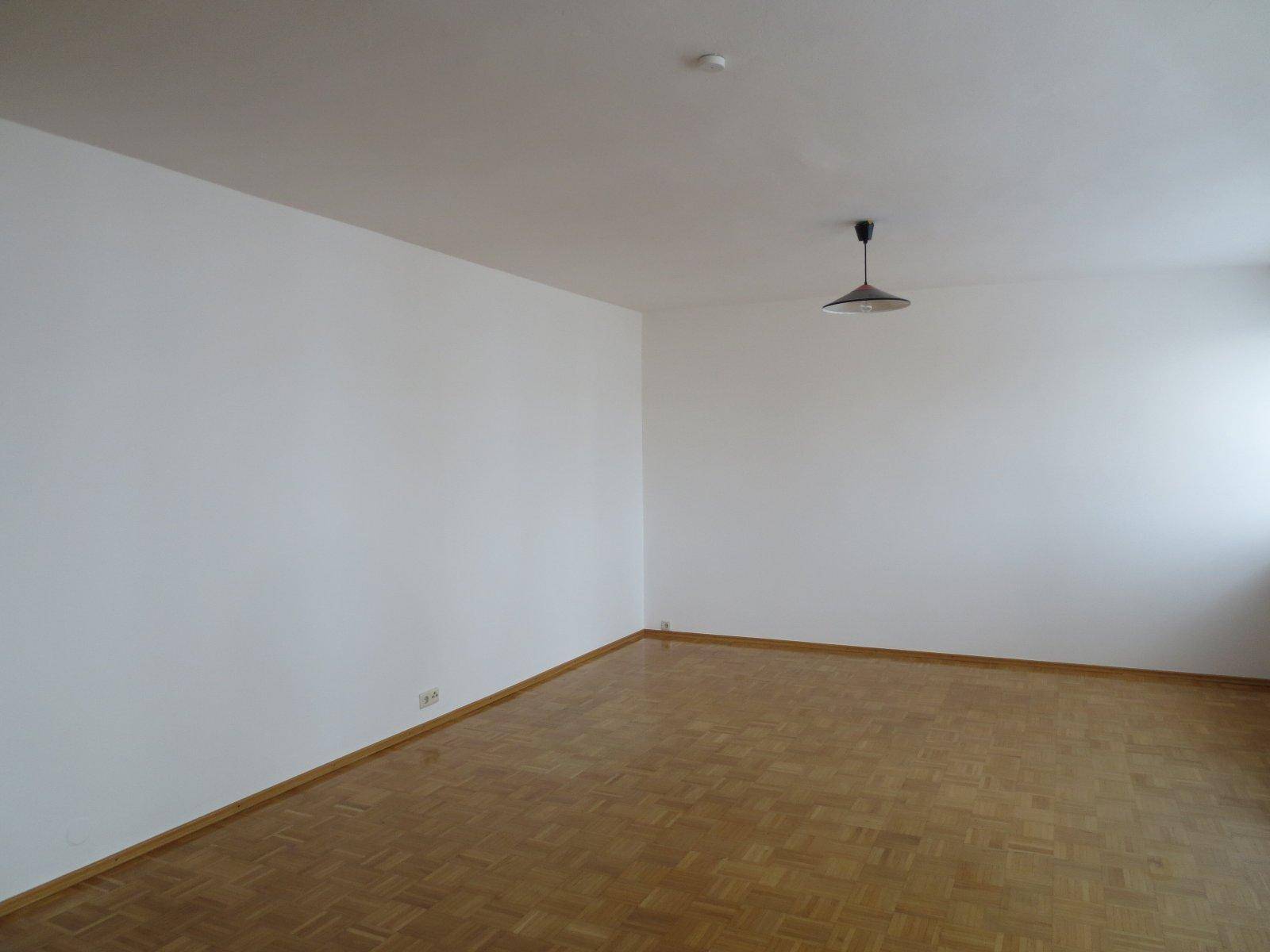 Geräumiges, leeres Zimmer mit Parkettboden und weißen Wänden, bereit zur Einrichtung.