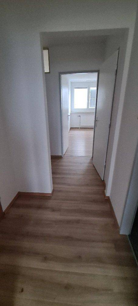 Heller Flur mit Laminatboden und weißen Wänden, der zu verschiedenen Zimmern führt.