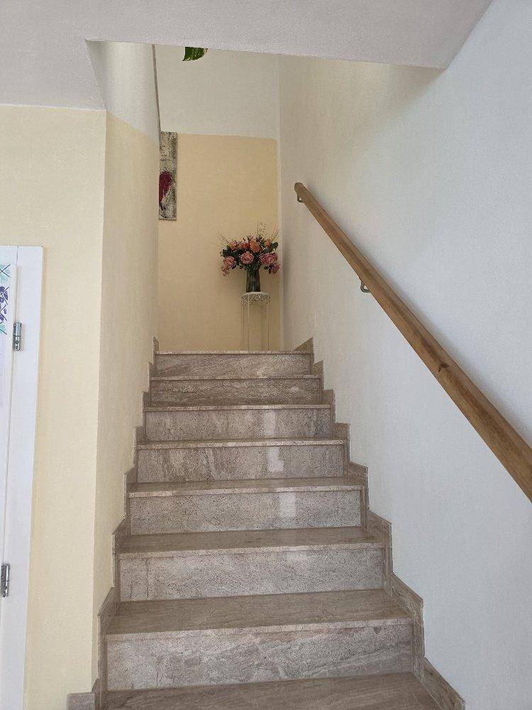 Marmortreppe mit Holzgeländer führt in die obere Etage, dekoriert mit Blumen.