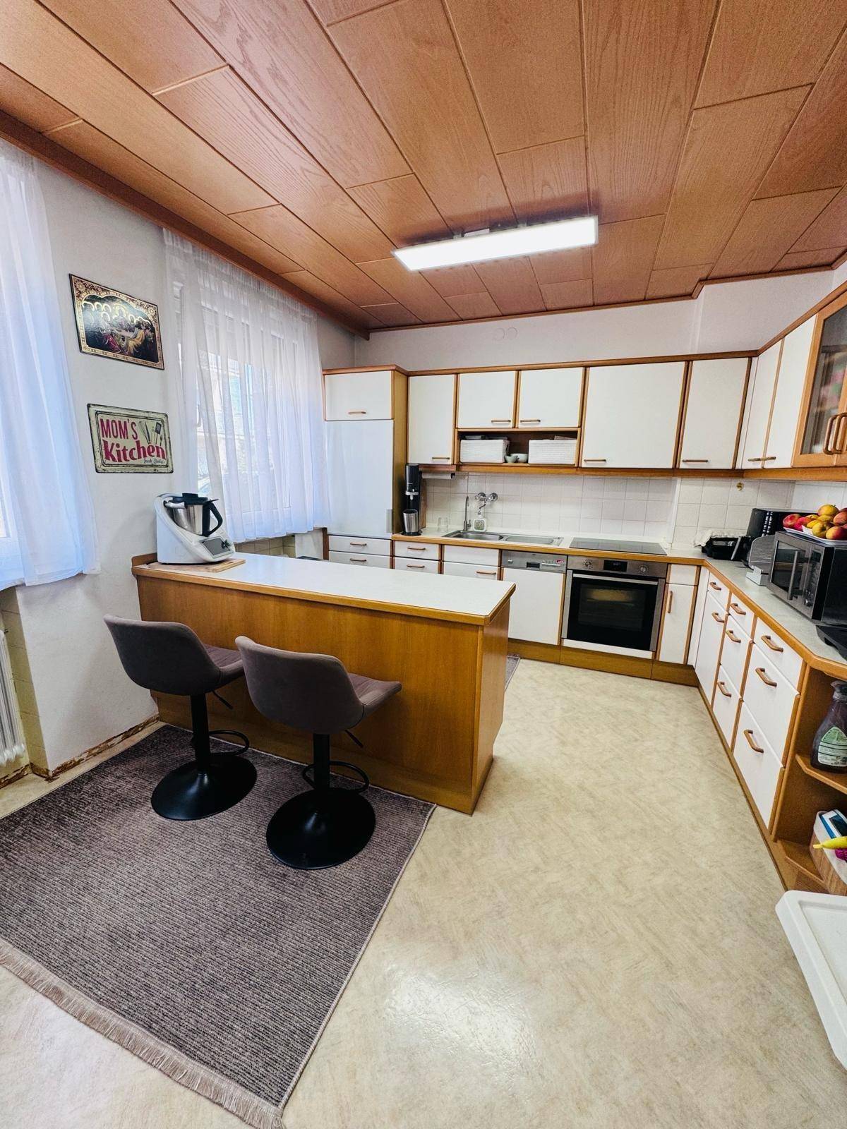 Funktionale Küche mit Holzdecke, weiß-braunen Schränken, Frühstücksbar und integrierten Geräten.