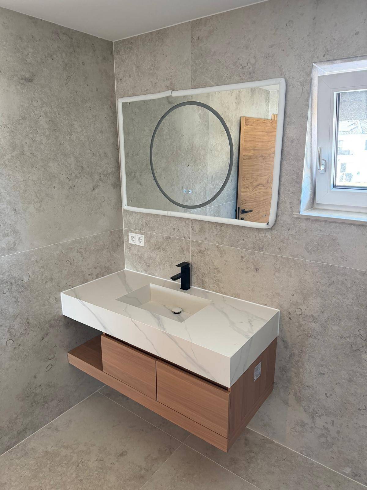 Modernes Badezimmer mit schwebendem Waschtisch, beleuchtetem Spiegel und grauen Wandfliesen.