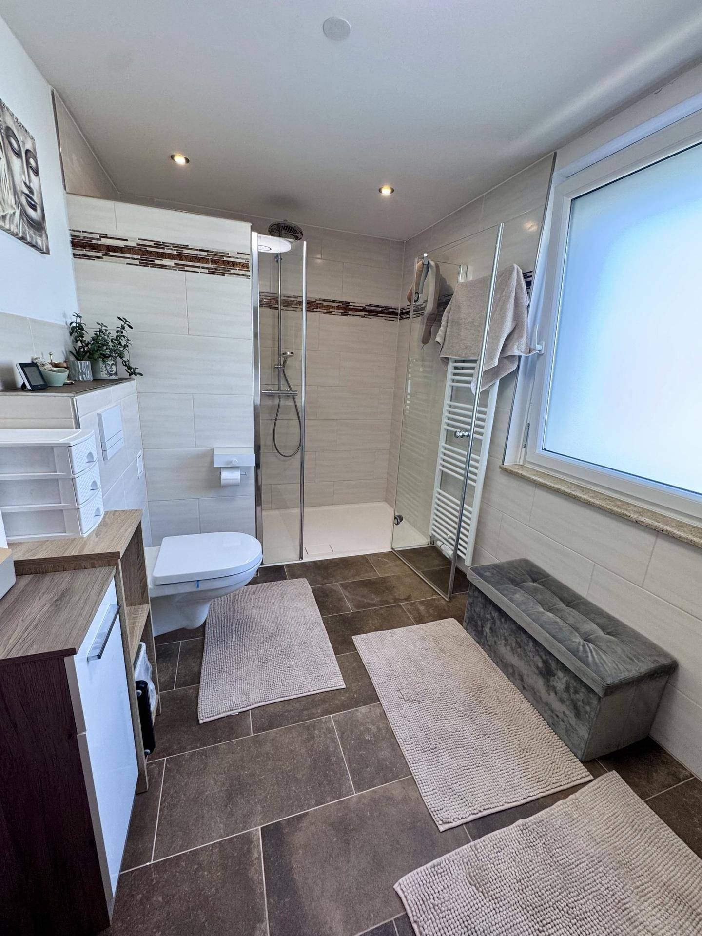 Modernes Badezimmer mit begehbarer Dusche, Wand-WC, Fenster und dunklen Bodenfliesen.