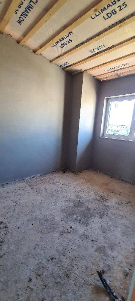 Unfertiges Zimmer mit sichtbaren Holzdeckenbalken und einem Fenster für Tageslicht.