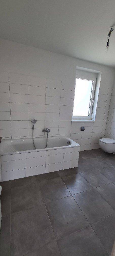 Modernes Badezimmer mit Badewanne, weißen Fliesen und Fenster für Tageslicht.